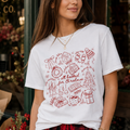 Woman wearing the All Booked for Christmas Comfort Colors 1717 graphic T-shirt featuring a cozy holiday doodle design with books, cocoa, ornaments, gifts, and festive Christmas illustrations.