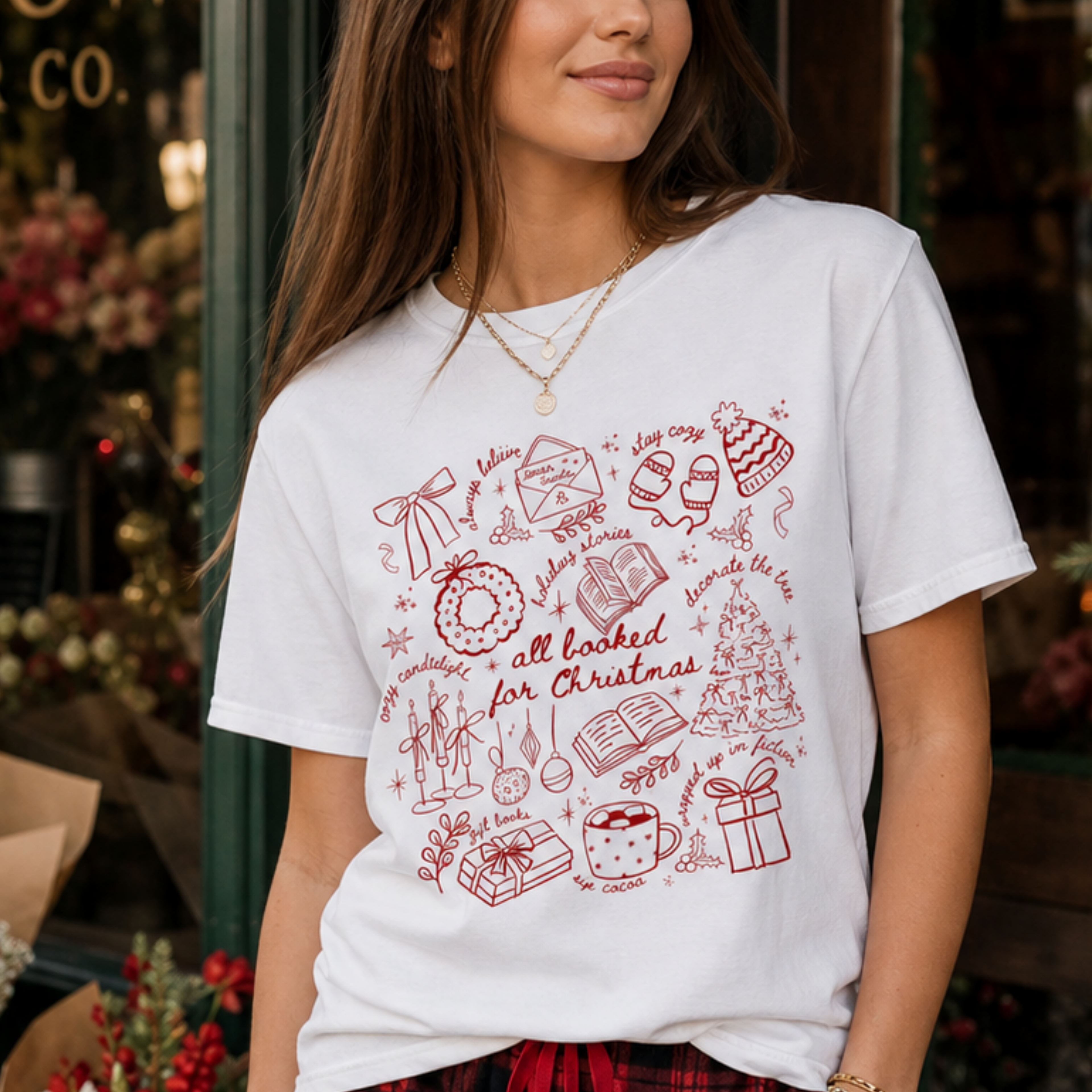 Woman wearing the All Booked for Christmas Comfort Colors 1717 graphic T-shirt featuring a cozy holiday doodle design with books, cocoa, ornaments, gifts, and festive Christmas illustrations.
